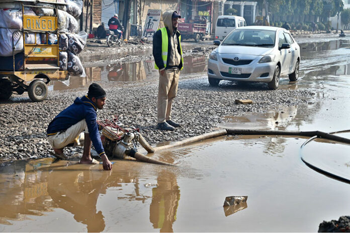 Workers use a motor pump to clear accumulated rainwater from the road, ensuring smoother passage for both traffic and pedestrians