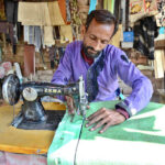 A tailor busy in sewing cushion cover for rickshaw body at his workplace