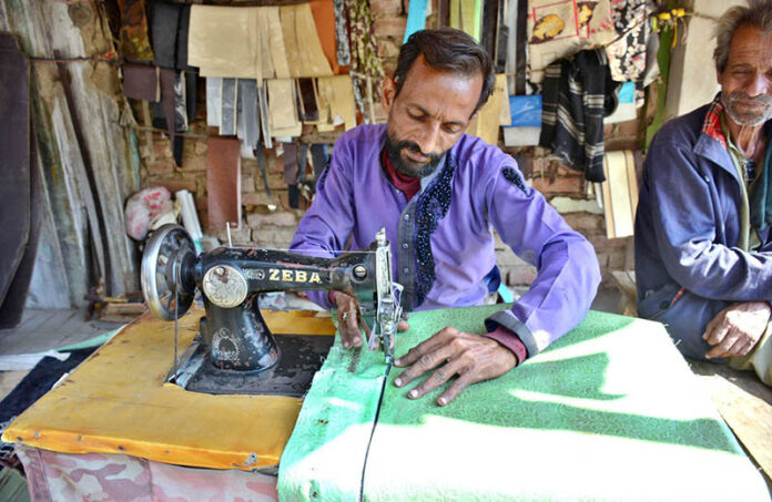 A tailor busy in sewing cushion cover for rickshaw body at his workplace