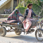 A woman covered with quilt to protect from chill weather while sitting on the tri-cycle rickshaw cart in the city