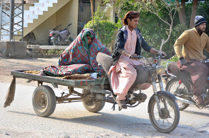 A woman covered with quilt to protect from chill weather while sitting on the tri-cycle rickshaw cart in the city