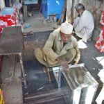 A skilled craftsman meticulously welds and assembles iron sheets, shaping them into sturdy boxes