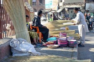 A customer carefully selects the best broom from a roadside vendor on the busy streets.