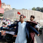 A vendor helps a customer try on a second-hand coat at his roadside setup at Bacha Khan Chowk