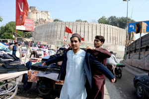 A vendor helps a customer try on a second-hand coat at his roadside setup at Bacha Khan Chowk