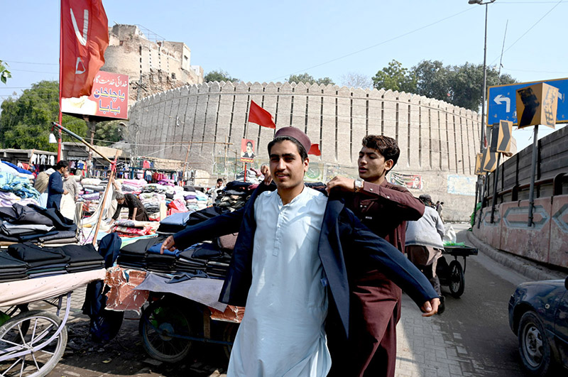 A vendor helps a customer try on a second-hand coat at his roadside setup at Bacha Khan Chowk