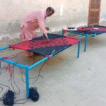 An artisan skillfully knitting a traditional charpai (woven bed) on the roadside in the city, earning his livelihood through this age-old craft