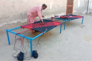 An artisan skillfully knitting a traditional charpai (woven bed) on the roadside in the city, earning his livelihood through this age-old craft