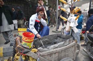 A vendor busy on his mobile phone, while waiting for customers to sell corn on his handcart in a local market.