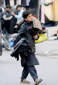 A young street vendor is displaying jackets while moving along the road at Hussain Agahi, aiming to attract customers and earn a livelihood through his sales