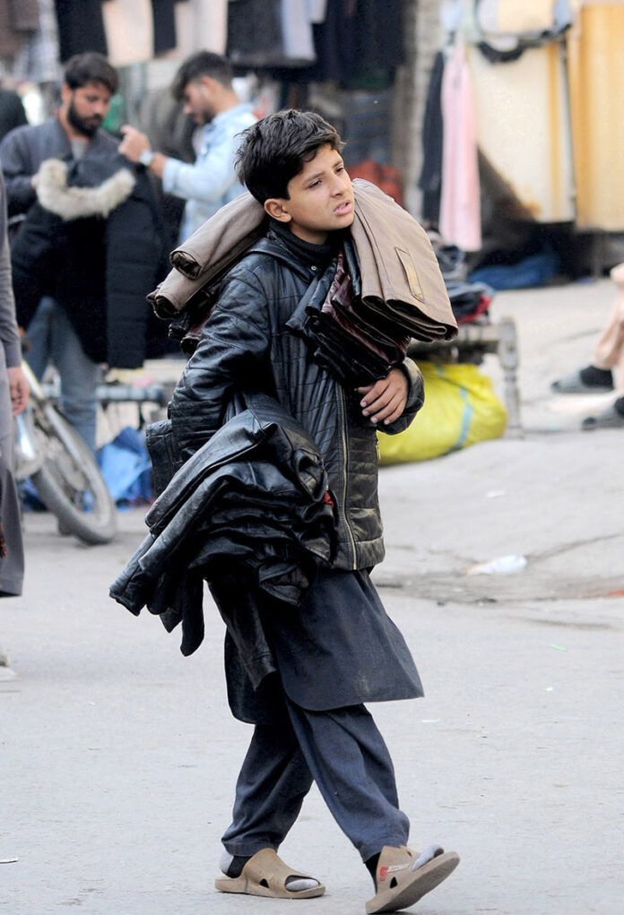 A young street vendor is displaying jackets while moving along the road at Hussain Agahi, aiming to attract customers and earn a livelihood through his sales