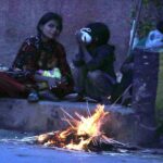 A woman with her kids sitting near the fire to keep them warm in the city at Court Road