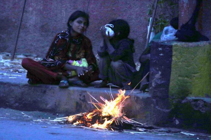 A woman with her kids sitting near the fire to keep them warm in the city at Court Road