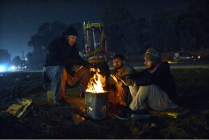 A group of people sitting around a crackling wood fire, seeking warmth and comfort as the winter chill envelops the Provincial Capital