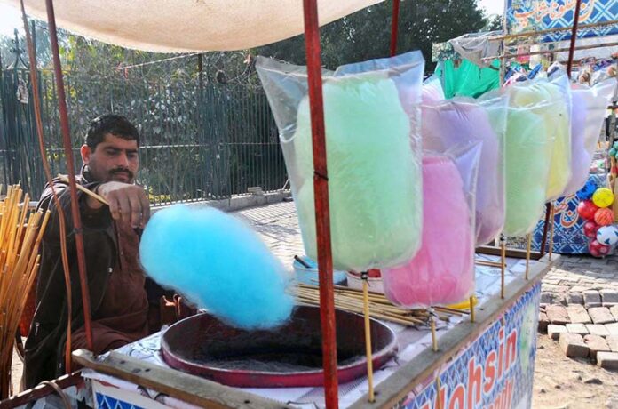 A vendor is busy preparing cotton candy at his roadside setup