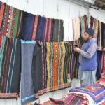 A vendor displays Balochi traditional shawls at his roadside setup, attracting passersby with the increased demand during the winter season at Liaqat Bazaar in the city