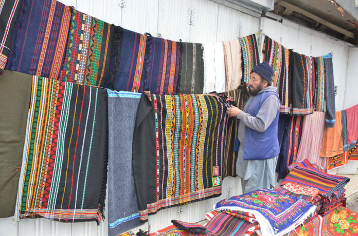 A vendor displays Balochi traditional shawls at his roadside setup, attracting passersby with the increased demand during the winter season at Liaqat Bazaar in the city