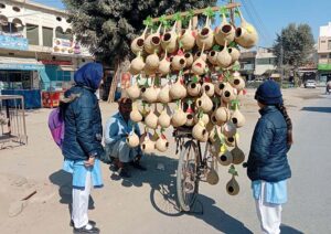 Two girls buy handmade dry grass nests for birds from a roadside stall.