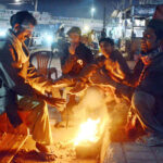 A group of people huddle around a crackling wood fire, finding warmth and comfort as the winter chill takes hold in city