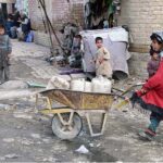 A small girl pushing a wheelbarrow to fetch water for home at Pishin Stop