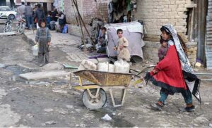 A small girl pushing a wheelbarrow to fetch water for home at Pishin Stop
