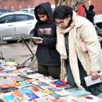 Women busy in selecting and purchasing old books from roadside stall at Mall Road