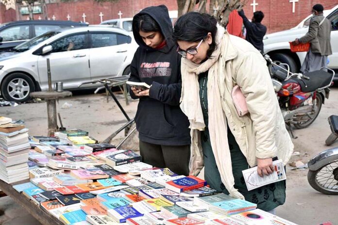 Women busy in selecting and purchasing old books from roadside stall at Mall Road
