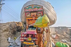 Laborers are carrying bags of chaff (husks from wheat) to load onto a vehicle at Latrar Road.