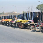 A customer explores a roadside stall for second-hand clothes at Khanna Pul, while fruit vendors line up nearby, offering fresh produce