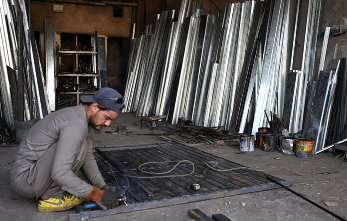 A welder diligently works on an iron gate at his workshop near Dhoke Kala Khan
