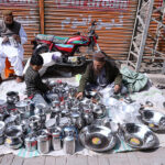 A street vendor meticulously arranges steel utensils at his roadside setup in Larkana, attracting customers with his neatly displayed collection