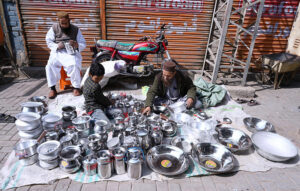A street vendor meticulously arranges steel utensils at his roadside setup in Larkana, attracting customers with his neatly displayed collection