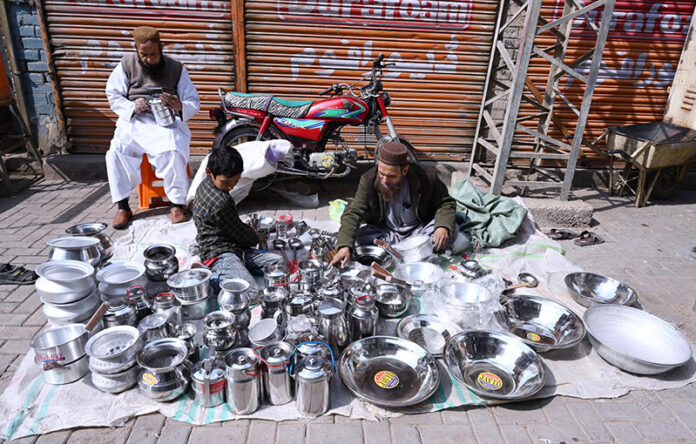 A street vendor meticulously arranges steel utensils at his roadside setup in Larkana, attracting customers with his neatly displayed collection