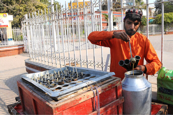 A vendor refills the mold of traditional Kulfi at his roadside stall, offering a refreshing and sweet treat to customers