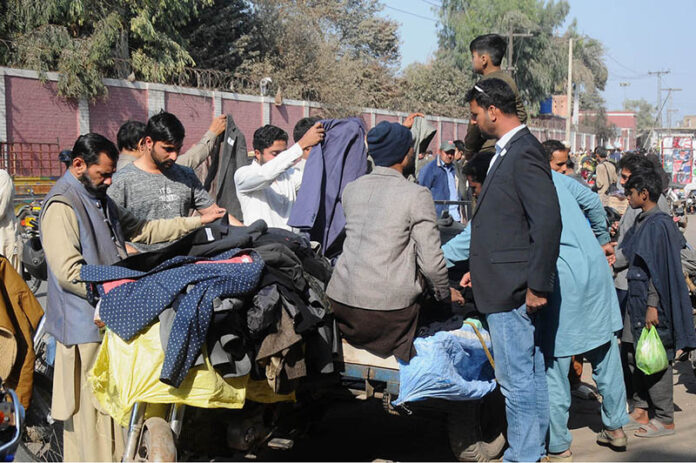 People selecting and purchasing second-hand coats from a roadside cart vendor