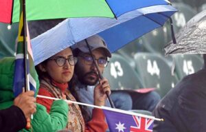 Cricket fans shield themselves with a plastic sheet, eagerly waiting for the rain to stop and play to resume in the ICC Champions Trophy match between Australia and South Africa at Rawalpindi Cricket Stadium.