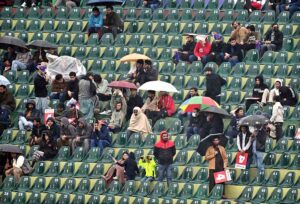 Cricket fans shield themselves with a plastic sheet, eagerly waiting for the rain to stop and play to resume in the ICC Champions Trophy match between Australia and South Africa at Rawalpindi Cricket Stadium.