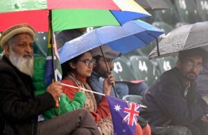 Cricket fans shield themselves with a plastic sheet, eagerly waiting for the rain to stop and play to resume in the ICC Champions Trophy match between Australia and South Africa at Rawalpindi Cricket Stadium.
