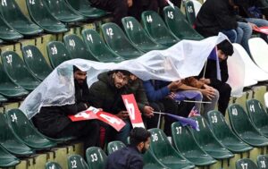 Cricket fans shield themselves with a plastic sheet, eagerly waiting for the rain to stop and play to resume in the ICC Champions Trophy match between Australia and South Africa at Rawalpindi Cricket Stadium.
