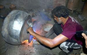 A worker puts the finishing touches to iron pots (digins) used for large banquets over a roaring fire at an iron factory near Mochi Gate.