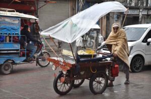 An aged man pushes a handcart with popcorn walks in rain to find customers.