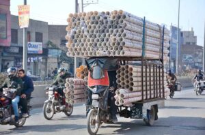 A tricycle loader on the way loaded with plastic pipes heading towards his destination.