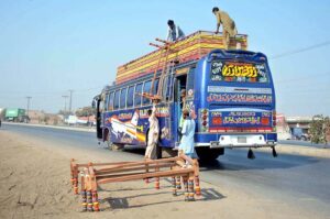 Laborers are busy loading frames of a traditional bed (charpai) on the roof of the Bus.