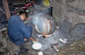 A worker carefully puts the finishing touches on iron pots (daigins) used for large banquets, heating them over a roaring fire at an iron factory near Mochi Gate.