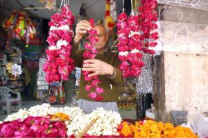 An aged person making flower garland for customer at Fawara Chowk