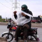 Bike rider is busy wear plastic sheet to cover himself from rain in the Federal Capital