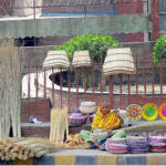 An elderly lady vendor making traditional brush brooms for the customers while sitting at her roadside setup