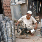 An elderly laborer skillfully crafts a steel bowl at his workplace