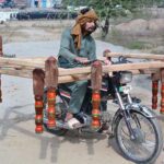 A carpenter carefully transports traditional wooden beds (charpai) on his motorcycle to sell them at another location