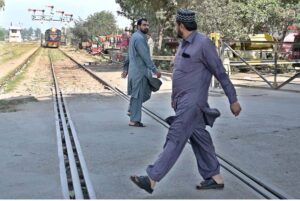 It is an extremely dangerous scene as two people are crossing the railway tracks while a train is approaching from behind, the authorities must intervene to prevent an accident if it occur.